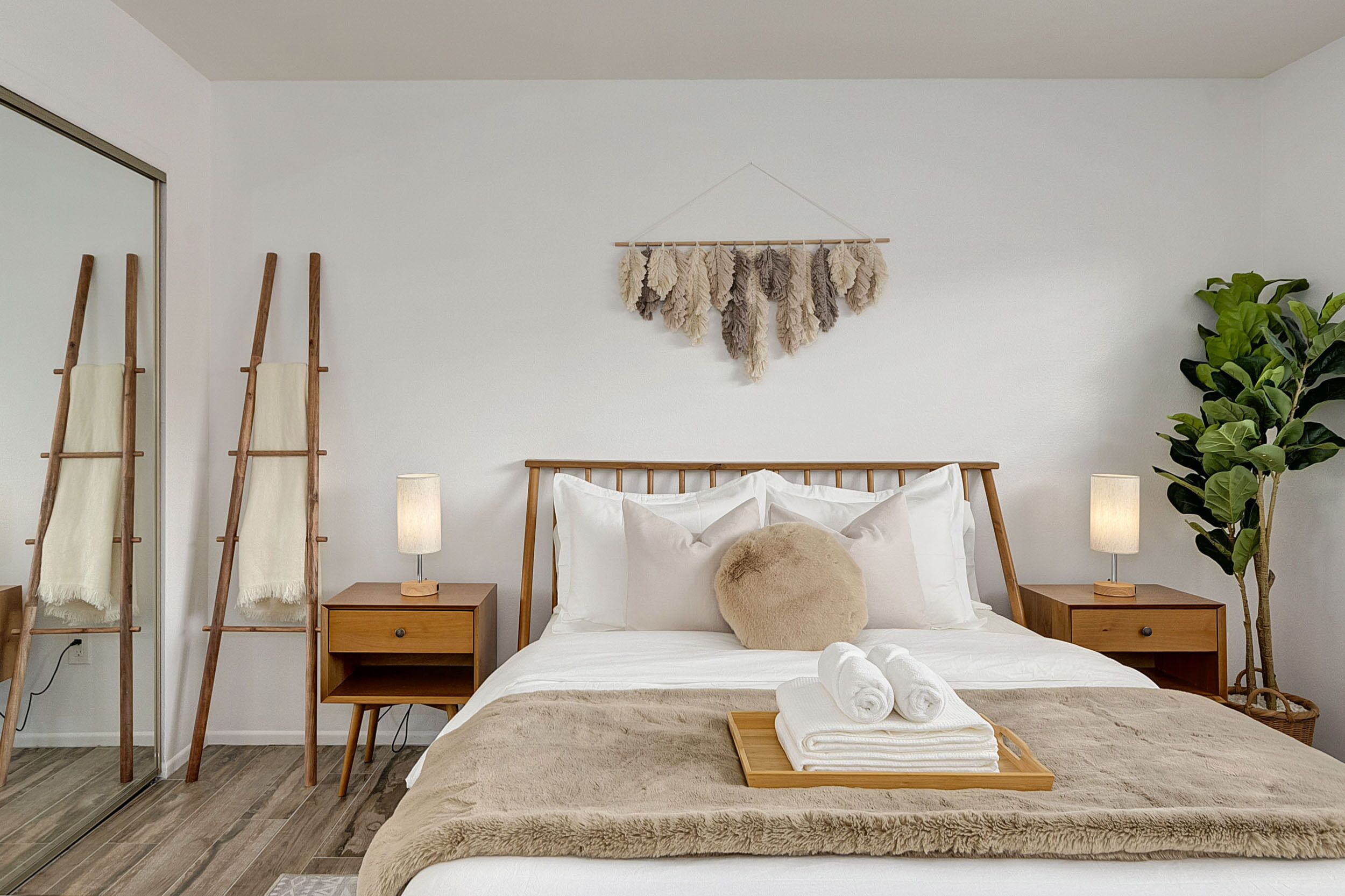 Un dormitorio con una cama de madera, dos mesitas de noche con lámparas, un espejo grande, una planta colgante y una alfombra mullida.