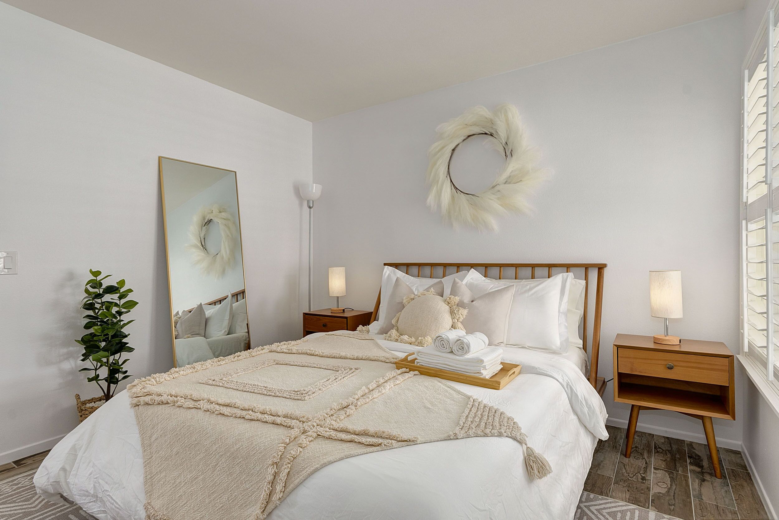 Um quarto bem arrumado com uma cama grande, uma mesinha de cabeceira com abajur, um espelho fixado na parede e uma guirlanda decorativa.