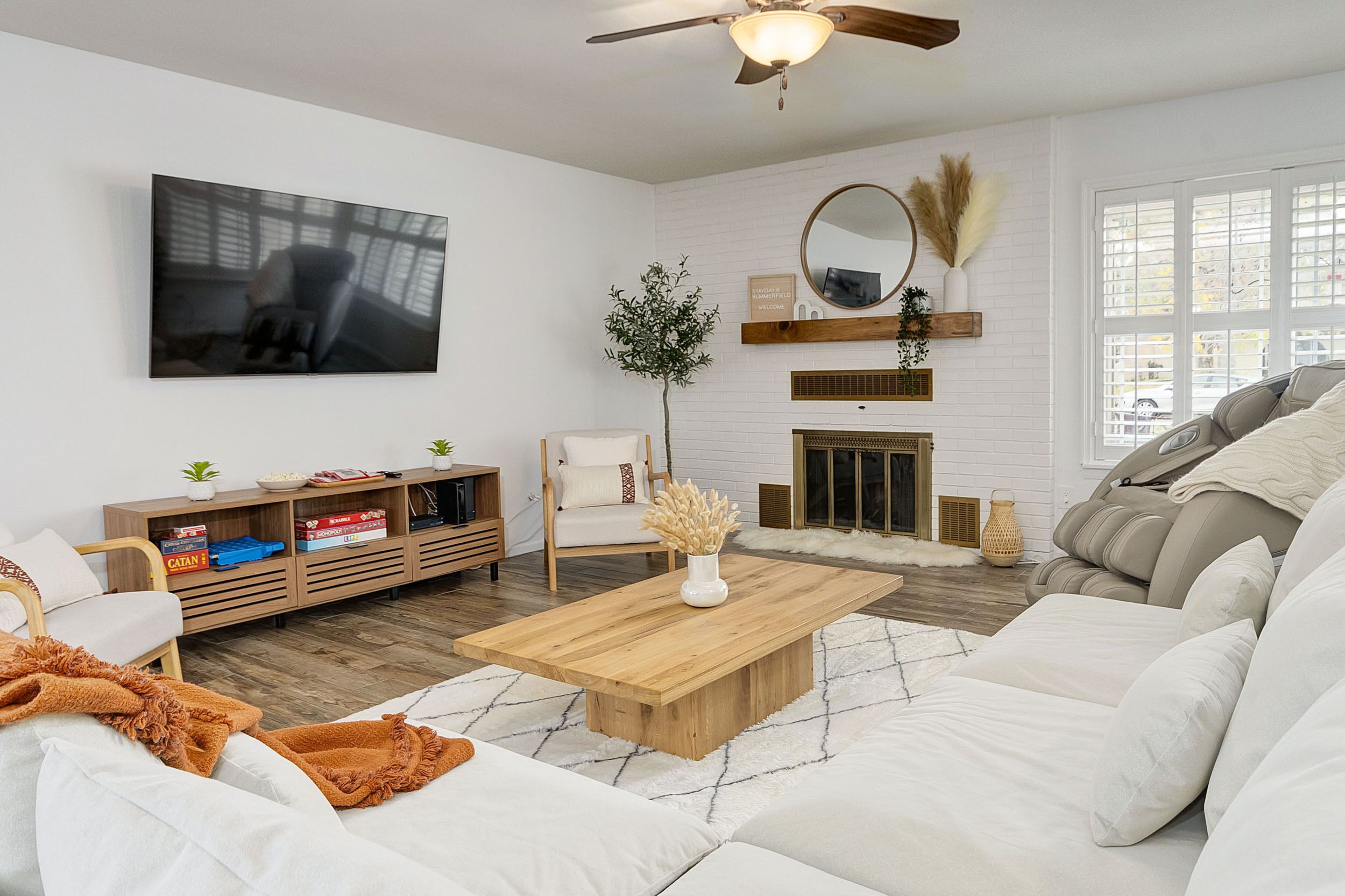A modern living room with a wooden coffee table, white sofas, a TV mounted on the wall, and a fireplace.