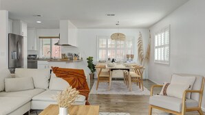 A modern kitchen with white cabinets, a stainless steel refrigerator, and a dining area with a wooden table and chairs.