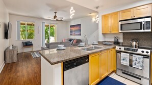 A modern kitchen with granite countertops, wooden cabinets, a built-in dishwasher, a stainless steel oven, and a microwave.