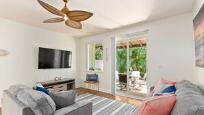 A modern living room with a grey sofa, a flat-screen TV, and a ceiling fan.