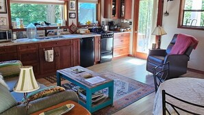A spacious living area with a wooden ceiling, a kitchen with a large window, and a dining area with a table and chairs.