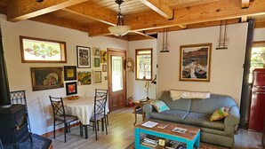 A cozy living room with a wooden ceiling, a dining table with chairs, a sofa with cushions, a coffee table, and a fireplace.