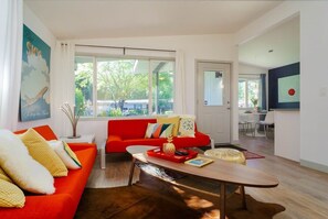 Una sala de estar moderna con un sofá rojo, una mesa de centro de madera y un ventanal con vistas a árboles.