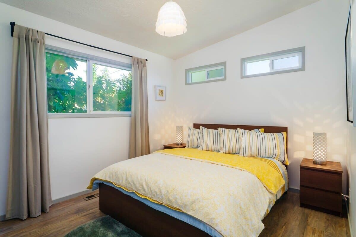 Une chambre à coucher comprenant un lit, deux tables de chevet, une fenêtre avec des rideaux et un luminaire au plafond.