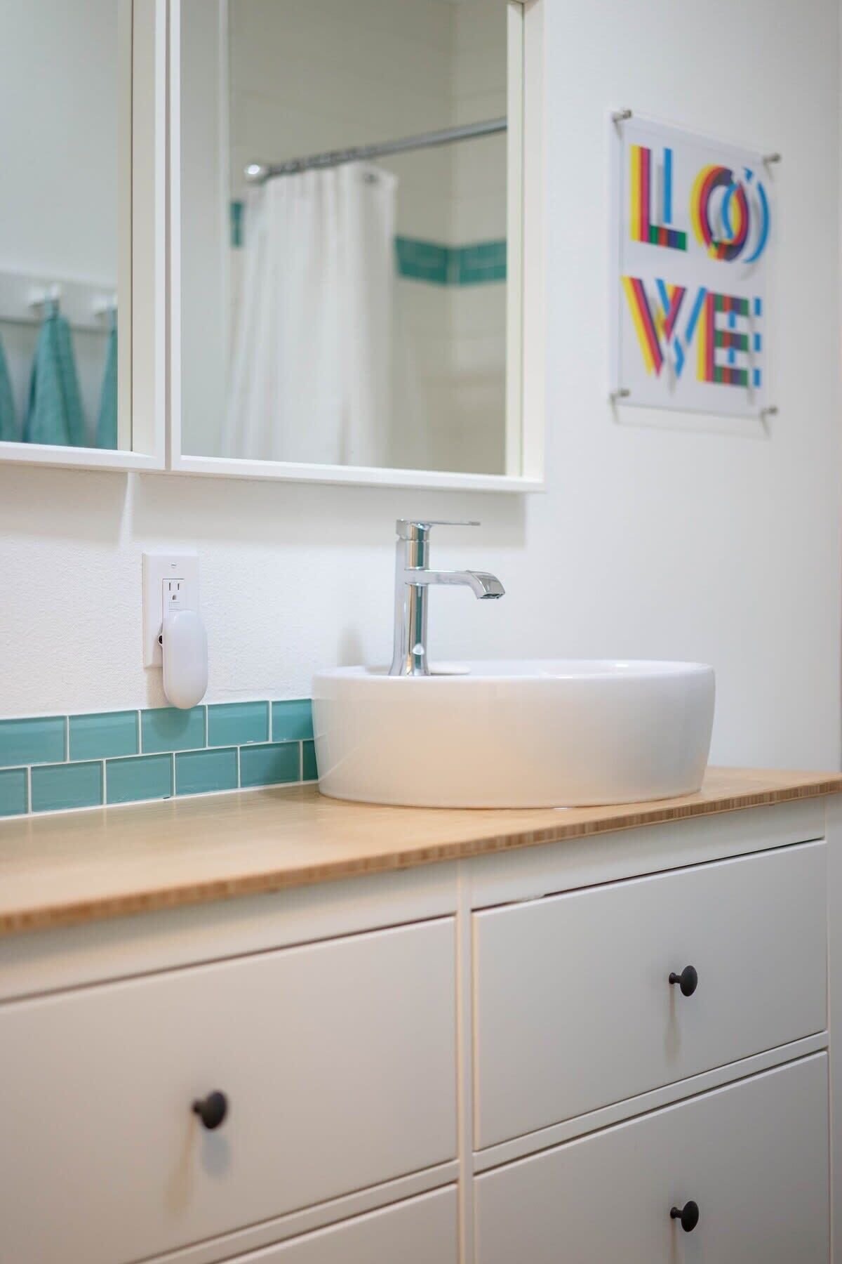 A bathroom with a white sink, a mirror, a towel rack, and a wall-mounted sign that reads 'LOVE'.