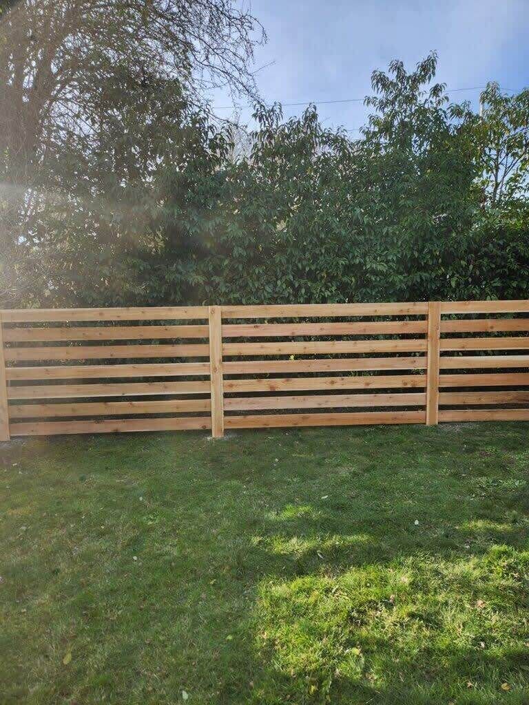 A wooden fence in a grassy area with trees in the background.