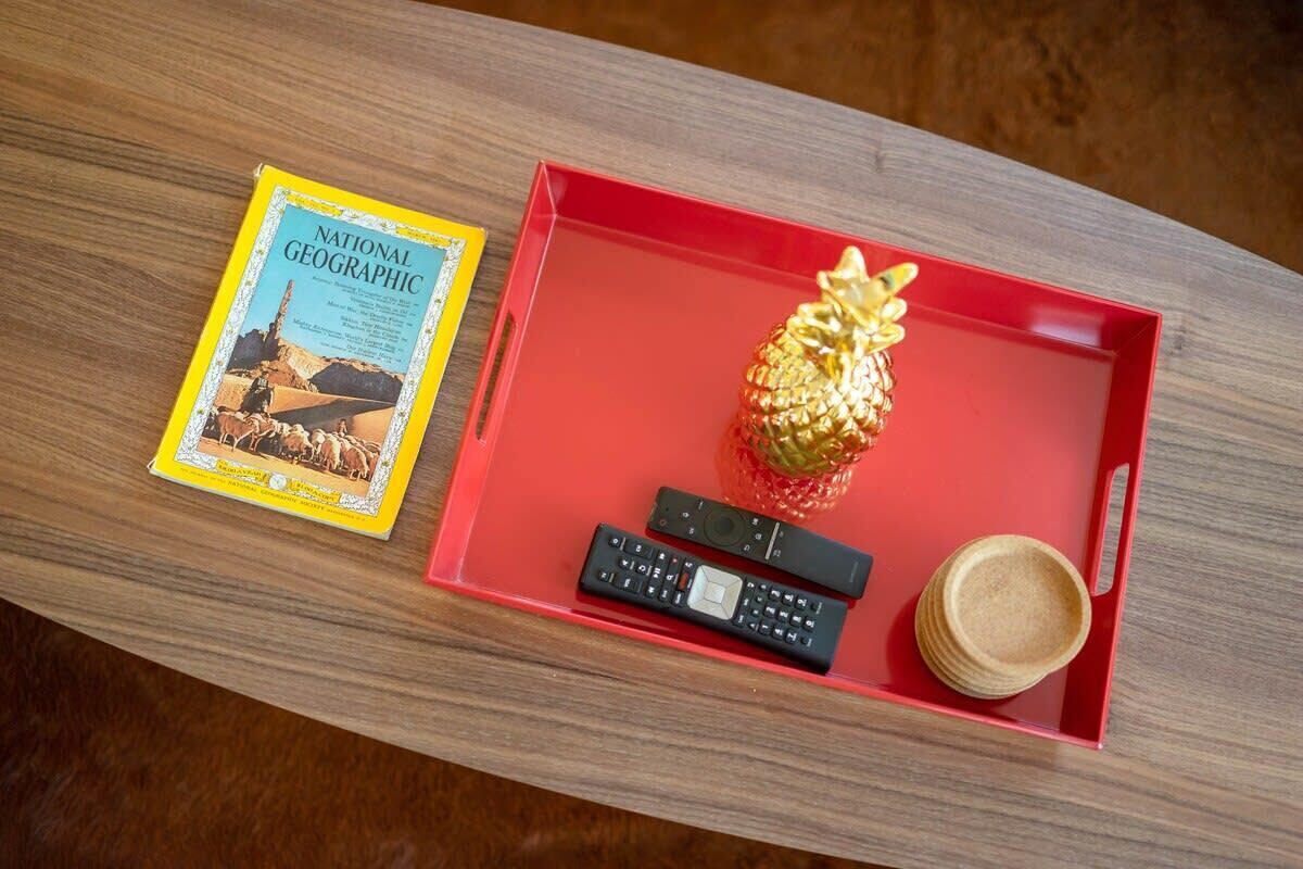 Una revista National Geographic, una bandeja roja con un adorno con forma de piña, dos controles remotos y una pila de tortitas.