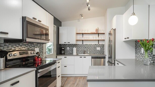 Une cuisine moderne avec des meubles blancs, un réfrigérateur en acier inoxydable et une bouilloire rouge posée sur la cuisinière.