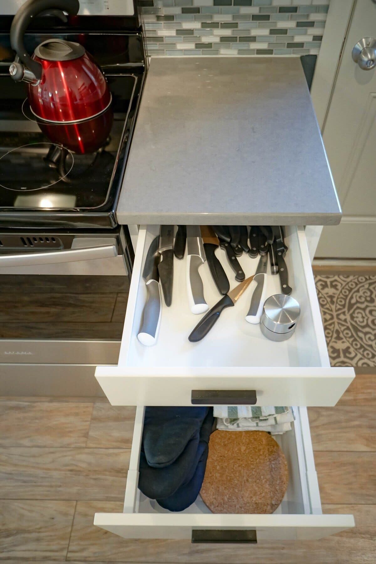 Una cocina con un cajón que contiene varios utensilios, una tetera roja y una hogaza de pan.