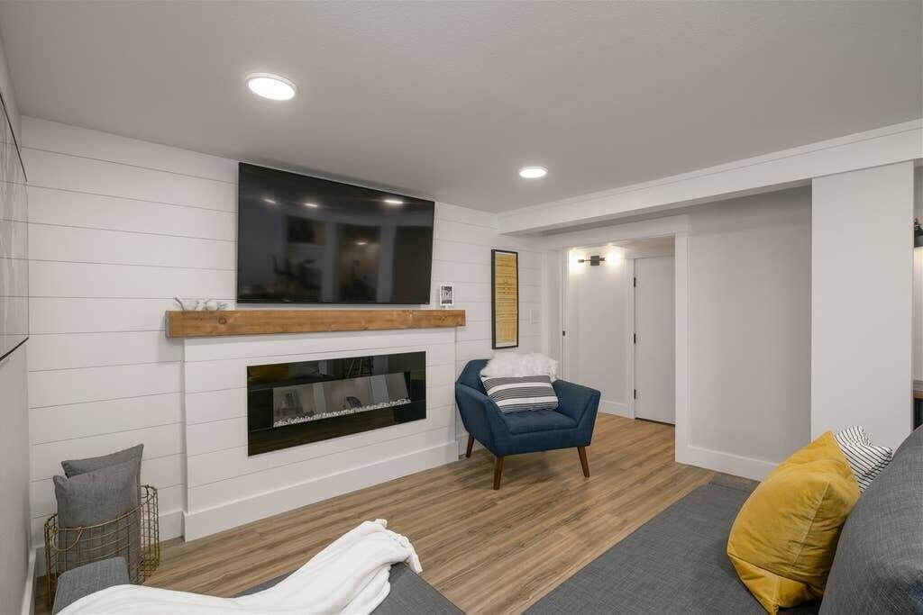 Een moderne woonkamer met een open haard, een blauwe fauteuil en een bank met een mosterdkleurig kussen.