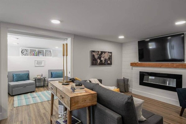 A modern living room with a grey sofa, a wooden coffee table, a flat-screen TV, and a fireplace.