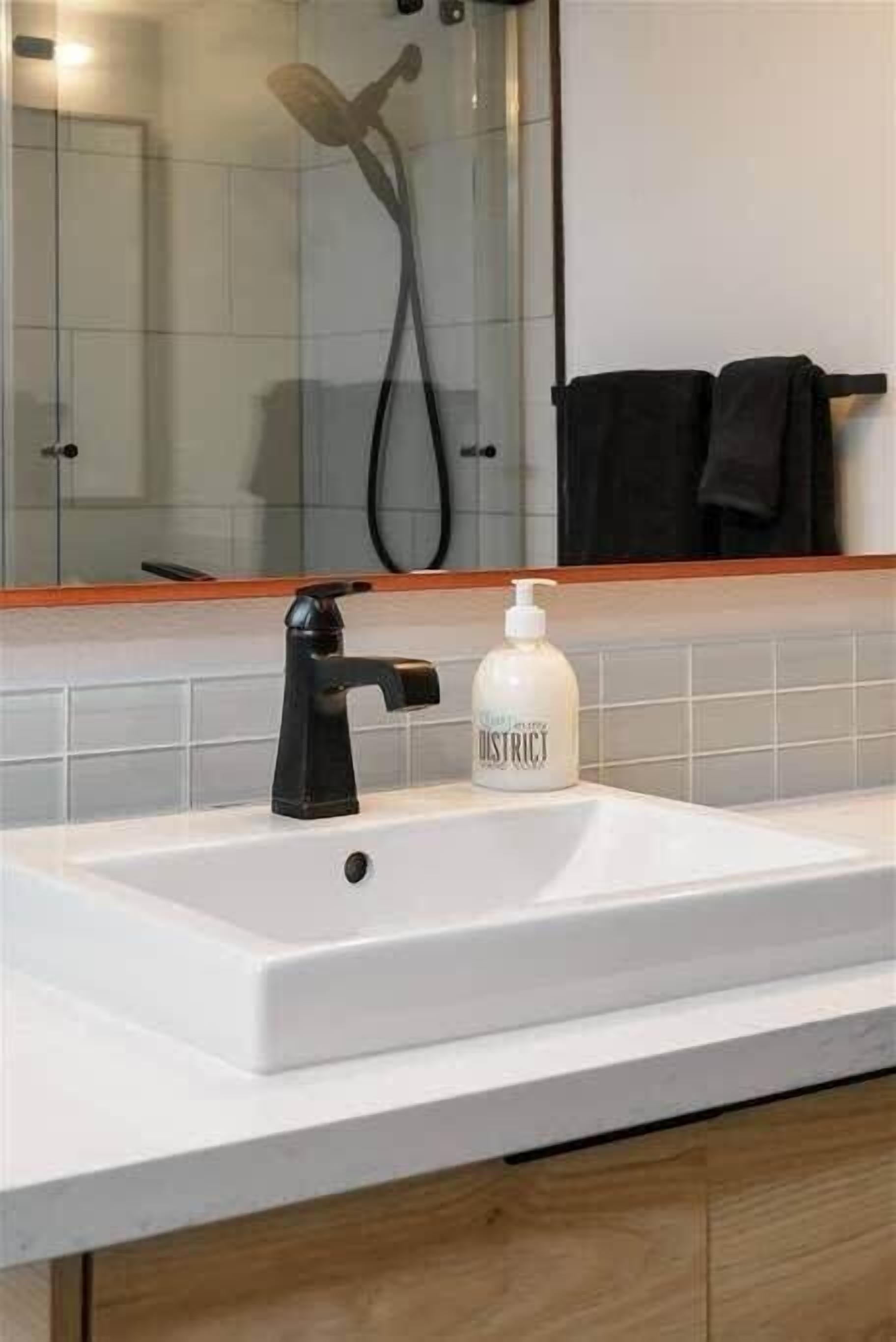 A bathroom with a white sink, black faucet, and a bottle of soap.