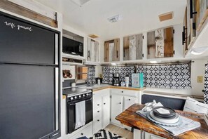 Une cuisine de taille réduite avec des meubles blancs, un réfrigérateur noir, une table à manger en bois et des carreaux décoratifs sur le mur derrière l’évier.