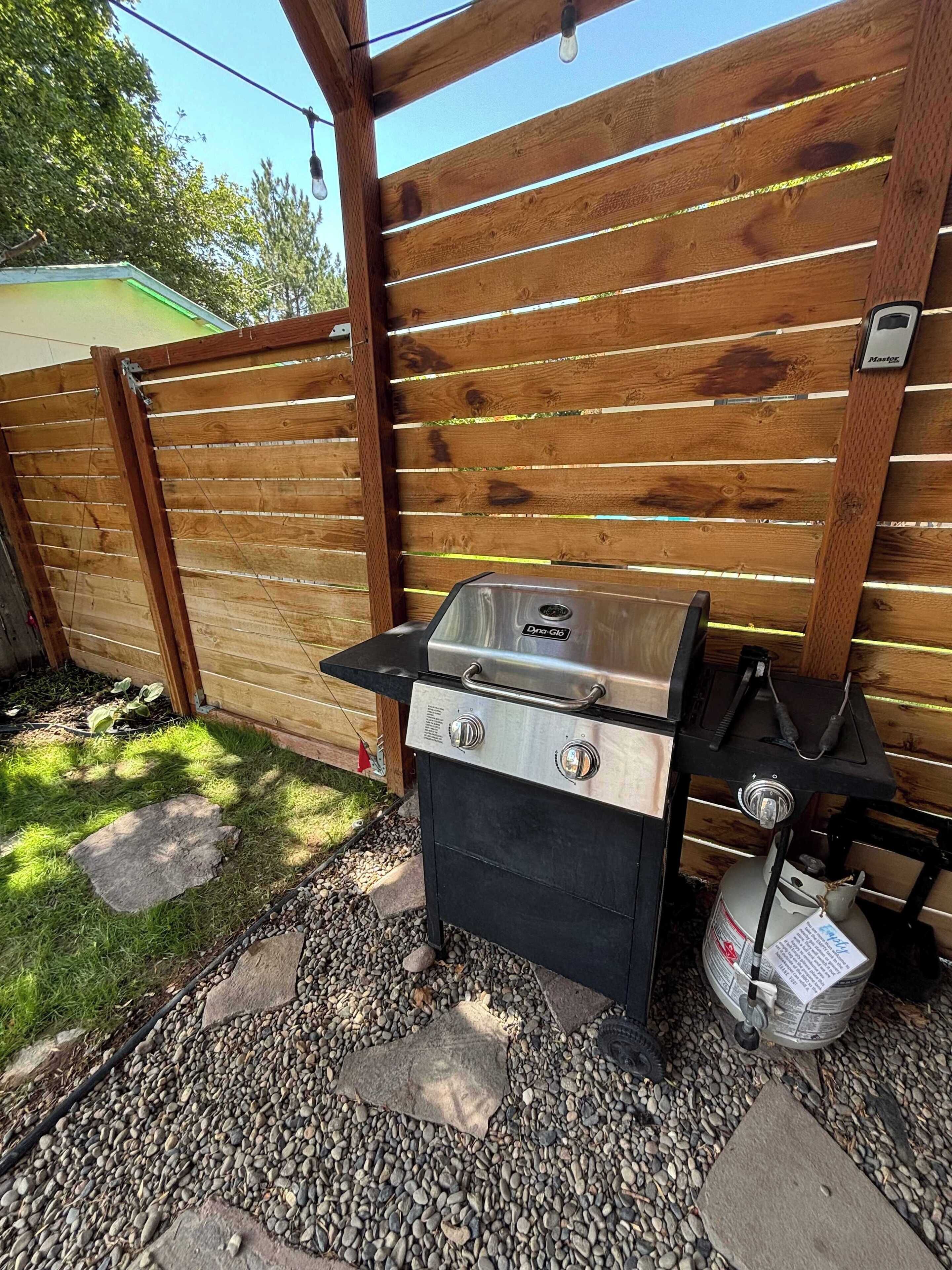 A backyard with a grill, a wooden fence, and a stone pathway.