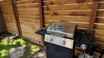 A backyard with a grill, a wooden fence, and a stone pathway.