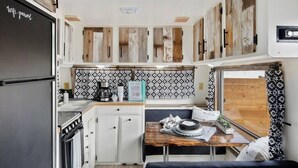 A compact kitchen with a stove, sink, and a dining area with a table and bench. - #StayinMyDistrict Twin Falls Backyard Glamper (Twin Falls)