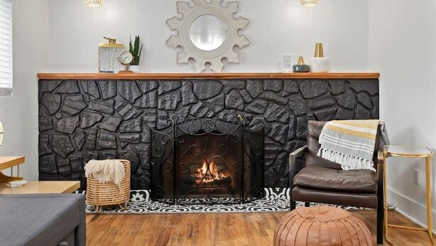 Un salon avec une cheminée en pierre, une table basse en bois, un fauteuil en cuir marron et une petite table d’appoint.