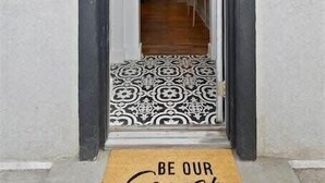 Une entrée moderne avec une porte à cadre noir, un paillasson à motifs et un paillasson sur lequel est écrit « Soyez les bienvenus ».