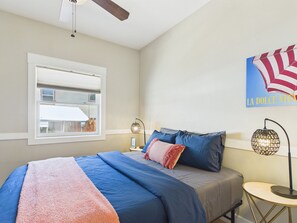A bedroom with a bed, a window, a ceiling fan, a wall clock, and a decorative piece.
