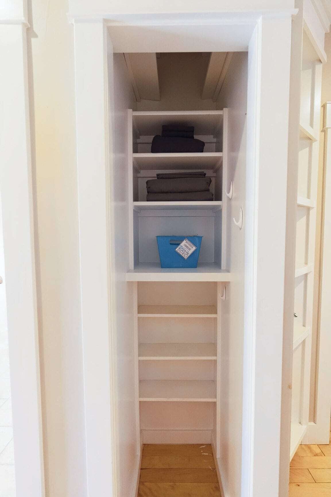 A white closet with shelves and drawers, a blue storage bin, and a wooden floor.