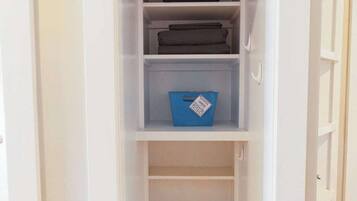 A white closet with shelves and drawers, a blue storage bin, and a wooden floor.