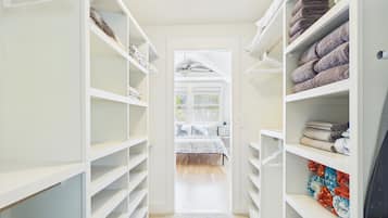 Un pasillo estrecho con estanterías blancas a ambos lados, que conduce a una habitación con cama y ventana.