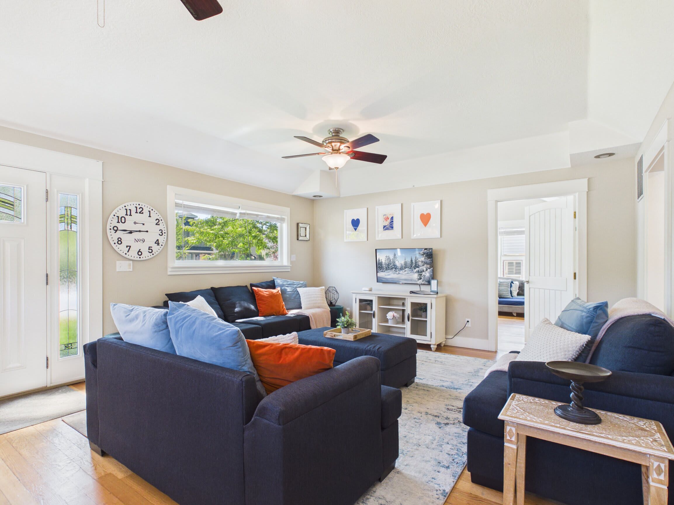 A modern living room with a ceiling fan, a large window, and a flat-screen TV.