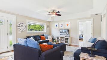 A modern living room with a ceiling fan, a large window, and a flat-screen TV.
