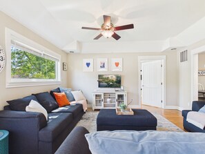 A living room with a sofa, TV, ceiling fan, and artwork on the wall.