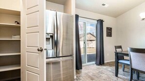 Cocina compacta con refrigerador de acero inoxidable, una mesa de comedor con sillas y una puerta corrediza de vidrio hacia un patio.