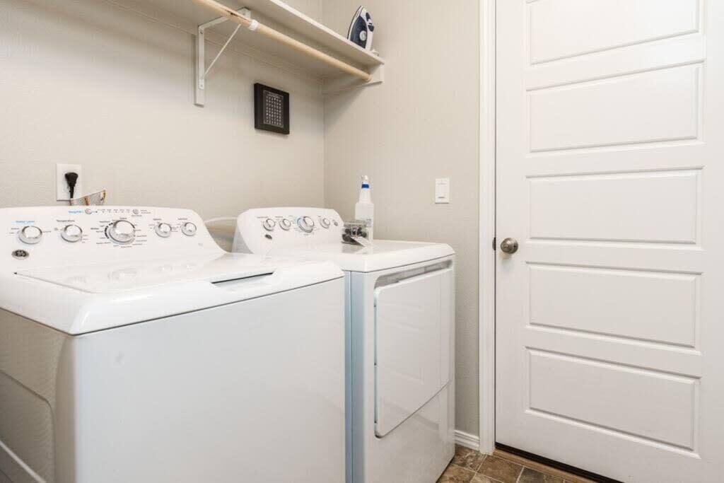 A laundry room with two white washers and dryers, a shelf above the dryers, and a white door.