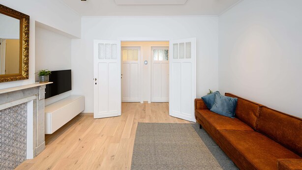 A modern living room with a wooden floor, a brown sofa, a flat-screen TV, a fireplace, and white doors leading to another room. - Stylish apartment in Middelkerke - 200m from the beach (Middelkerke)