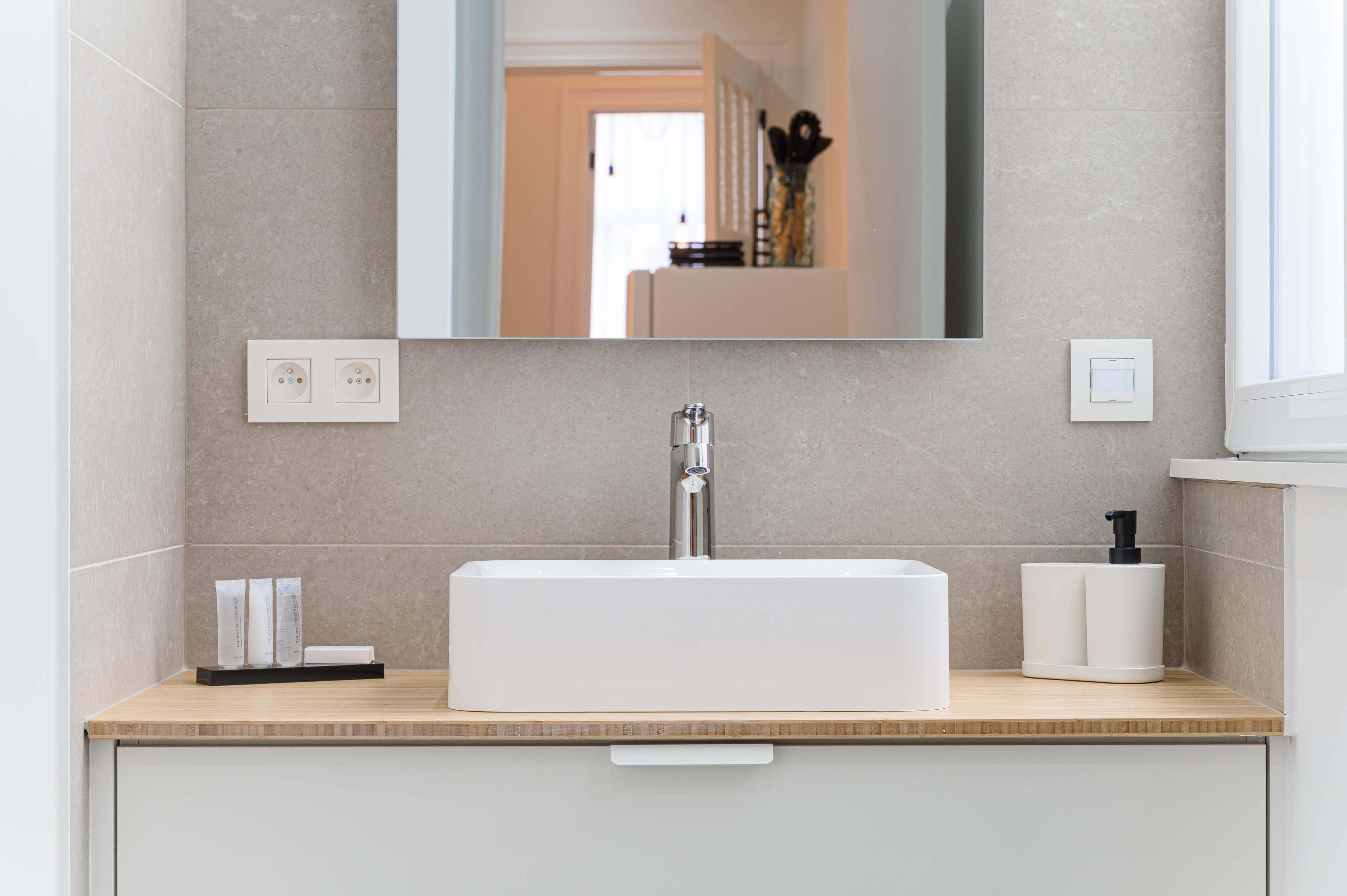 A modern bathroom with a white sink, a mirror, and a towel dispenser.