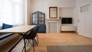 A room with a wooden dining table, black chairs, a blue cabinet, a fireplace, a TV, and a white door. - Stylish apartment in Middelkerke - 200m from the beach (Middelkerke)