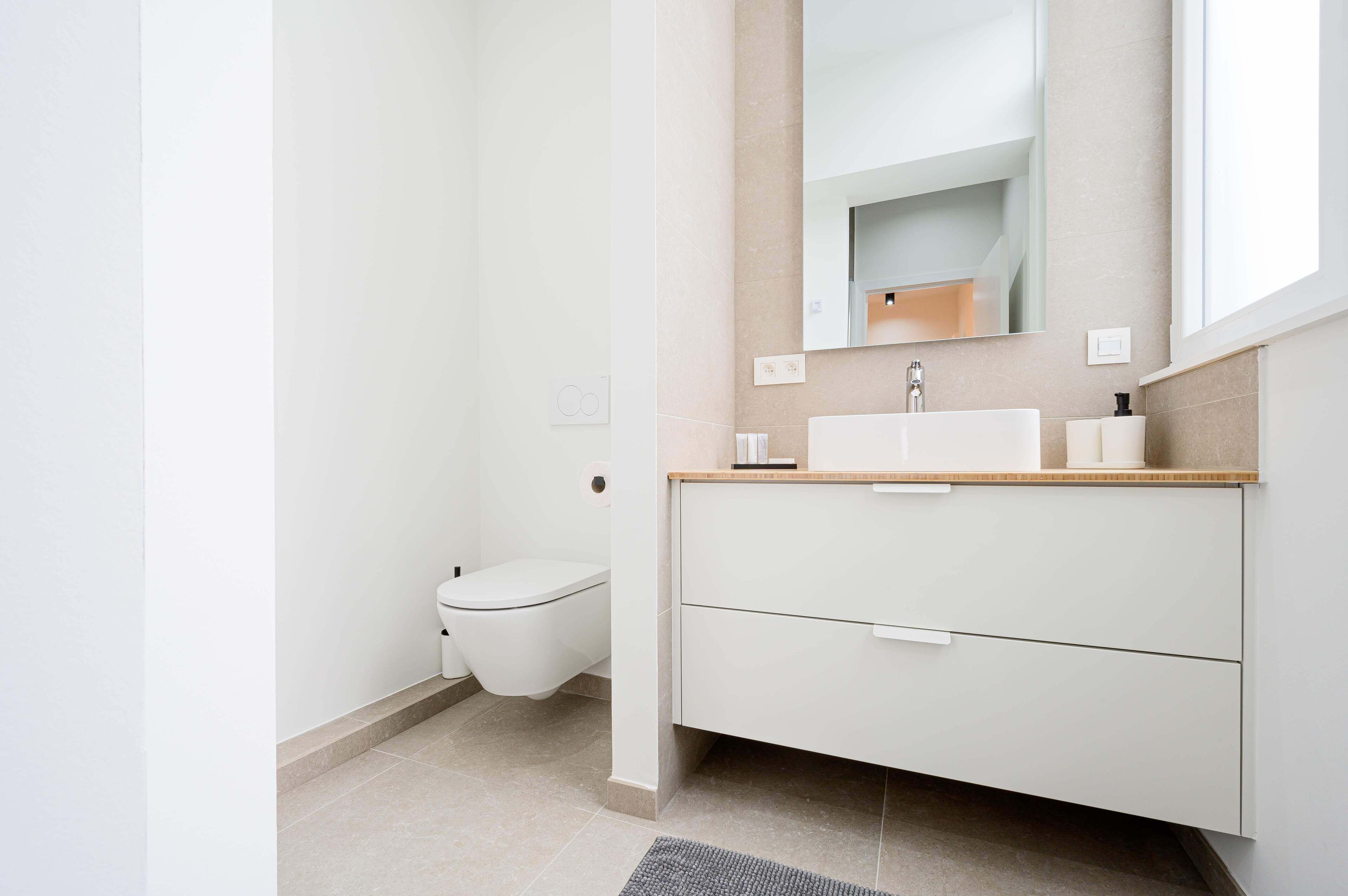 A modern bathroom with a white toilet, a sink with a mirror above it, and a beige countertop.