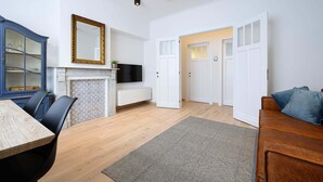 A modern living room with a wooden dining table, black chairs, a blue cabinet, a fireplace, a TV, and a large mirror. - Stylish apartment in Middelkerke - 200m from the beach (Middelkerke)