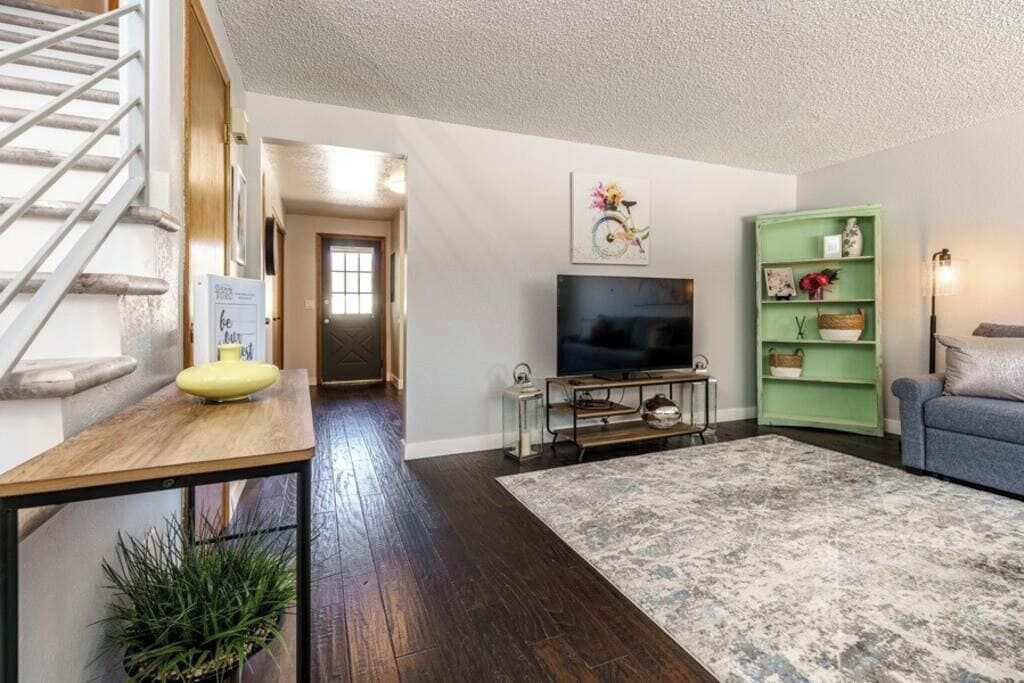 A living room with a TV, a green shelf, a blue sofa, and a staircase.