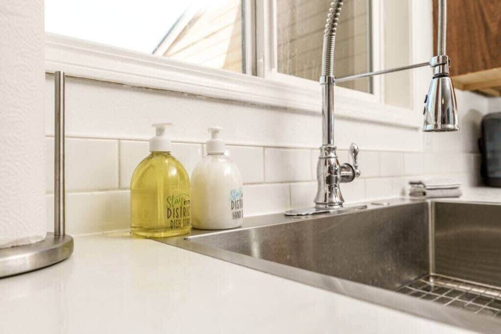 Uma cozinha com pia de aço inoxidável, uma torneira e duas garrafas de detergente sobre o balcão.