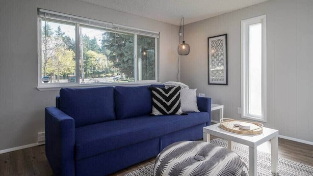 Un salon moderne avec un canapé bleu, une petite table blanche et un pouf à motifs.