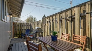Une terrasse en bois avec une table et des chaises, un barbecue et un pot de fleurs.