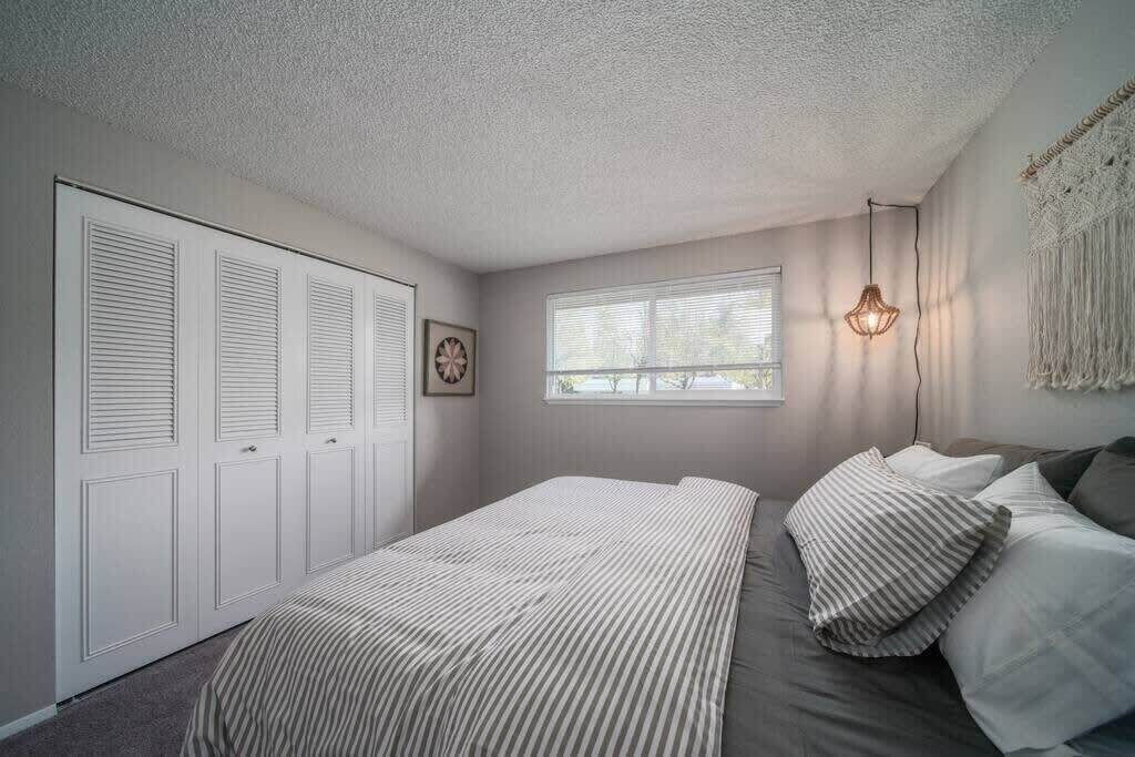 A bedroom with a bed, a window, a wall-mounted light fixture, and a door with louvered panels.
