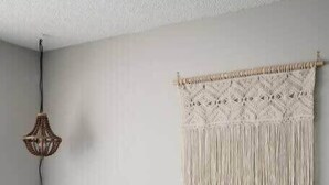 Une chambre avec un lit, une décoration murale en macramé, une petite table avec une lampe et un luminaire fixé au mur.