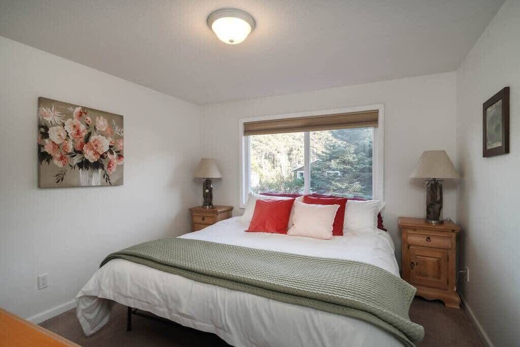 Une chambre à coucher avec un lit, une fenêtre donnant sur un beau paysage, un tableau accroché au mur et deux tables de chevet avec des lampes.