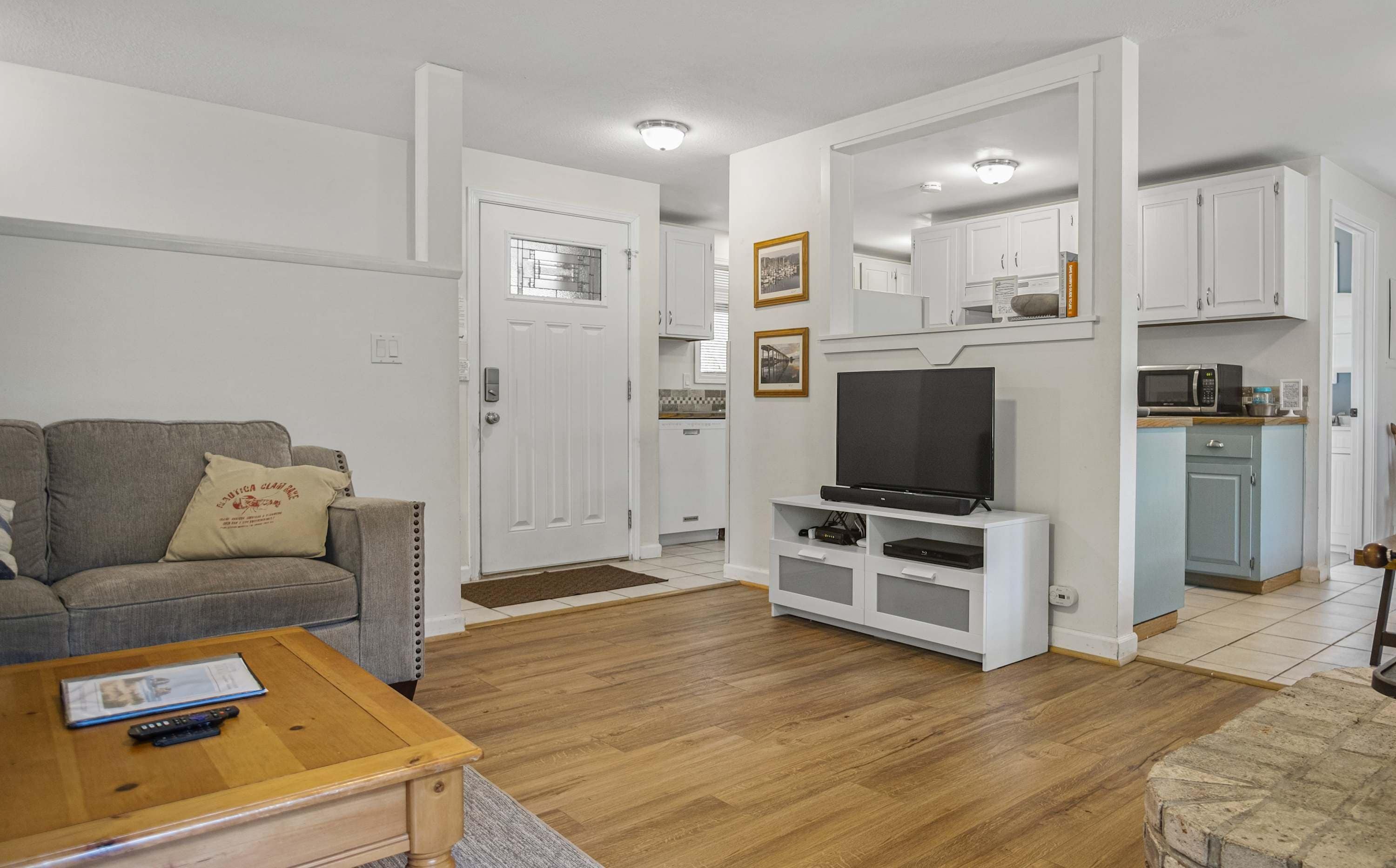 Una sala de estar con sofá, mesa de centro, televisor y un área de cocina con armarios y microondas.