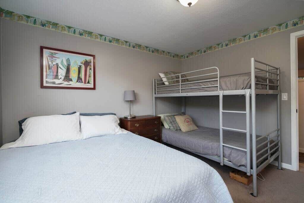A bedroom with a single bed, a bunk bed, a nightstand, a lamp, and a framed picture on the wall.
