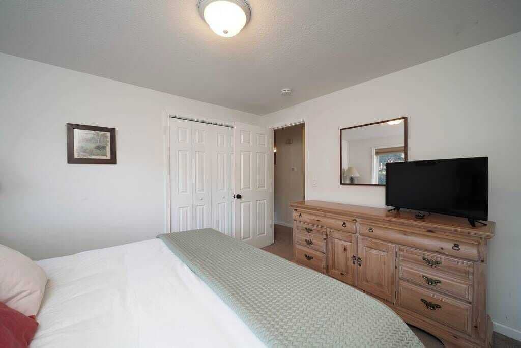 A bedroom with a bed, a dresser, a television, and a door.