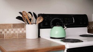 Una cocina con un horno blanco, un hervidor verde y un recipiente blanco que contiene utensilios de madera.