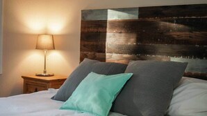 Una cama con ropa blanca, dos almohadas, una lámpara de noche y un cabecero de madera.